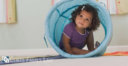 child sitting in play tunnel looking up and out