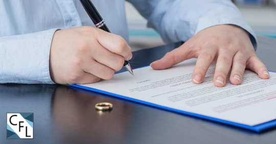 man signing paperwork with wedding ring on the table