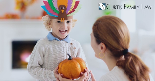 kid holding pumpkin wearing a turkey headband and mom smiling